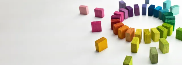 Bunte Holzbausteine in Regenbogenfarben, die auf weissem Grund wellenförmig angeordnet sind und sich zu einem Kreis verbinden.