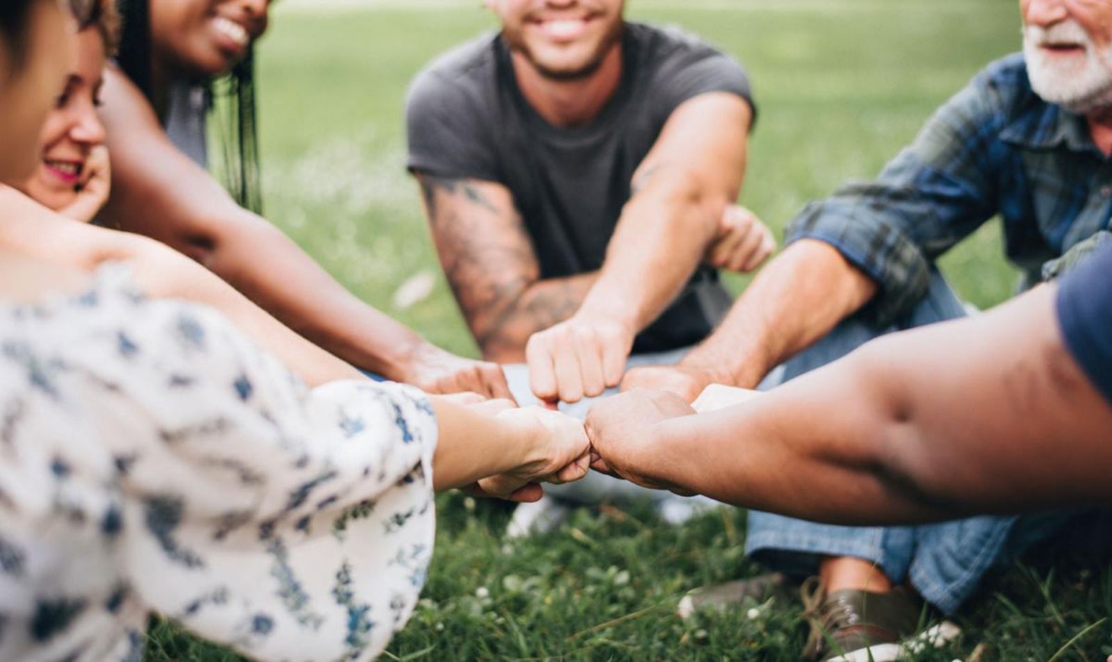 Eine Gruppe von Menschen  sitzt im Gras zeigt durch Faustgesten Gemeinschaft und Zusammenhalt.