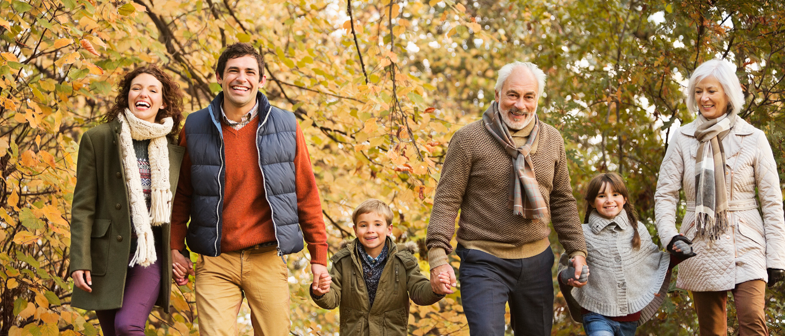 Eltern, Kinder und Grosseltern spazieren in einer herbstlichen Landschaft.